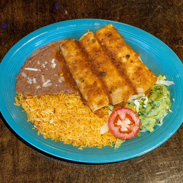 Los Mariachis Mexican Restaurant Jenks' enchiladas with rice, refried beans, guacamole, and tomato on a blue plate.