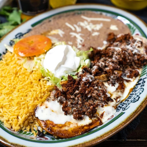 A Mexican dish with rice, refried beans, a tomato slice, sour cream, and meat covered in cheese sauce.