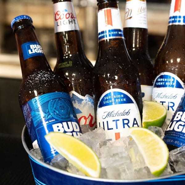 An ice bucket filled with various beer bottles, including Bud Light, Coors Light, and Michelob Ultra, with lime wedges.