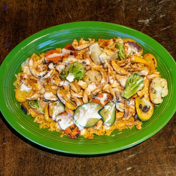 Grilled chicken and vegetables, including zucchini, broccoli, and carrots, over rice on a green plate.