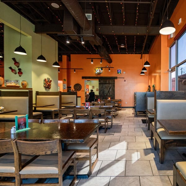 Spacious dining room at Los Mariachis Mexican Restaurant with orange and green walls, tables, and booths.