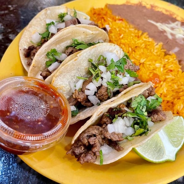 Four street tacos with steak, onions, and cilantro, served with rice, beans, salsa, and lime.