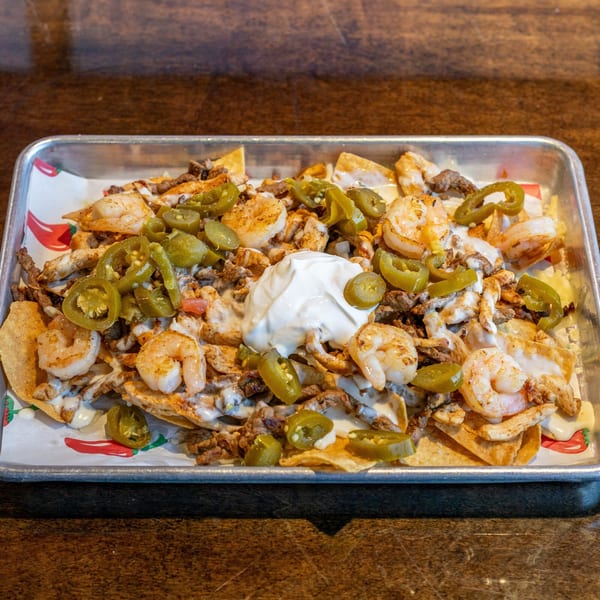 A tray of Los Mariachis Mexican Restaurant nachos with shrimp, steak, jalapeños, and sour cream.