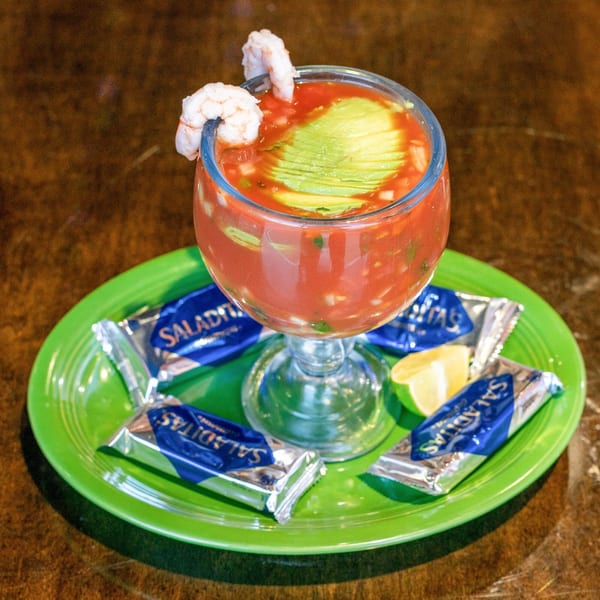 Shrimp cocktail with avocado slices and lime on a green plate with Saladiitas crackers.
