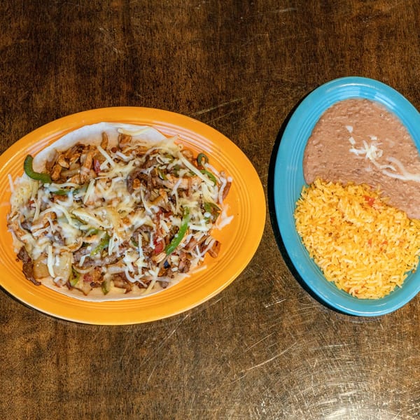 Los Mariachis' fajita burrito with melted cheese, rice, and refried beans on a wooden table.