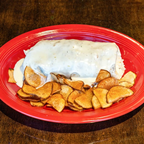 A large burrito covered in white sauce, served with seasoned potato slices on a red plate.