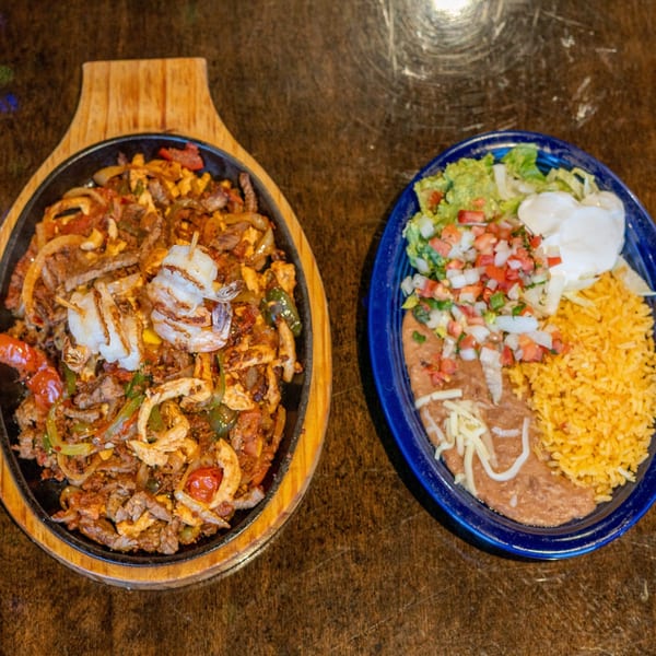 Sizzling fajitas with shrimp, steak, and chicken, alongside a plate of rice, beans, and guacamole.